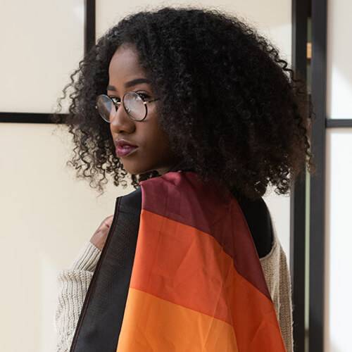 A Black femme drapes a Pride flag across their shoulder.