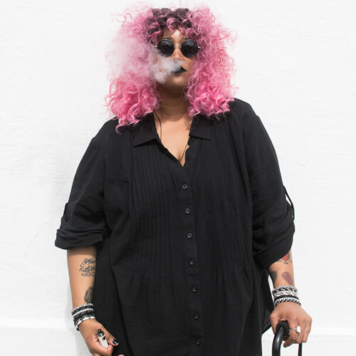 A Black non-binary person holds a cane and vape pen.